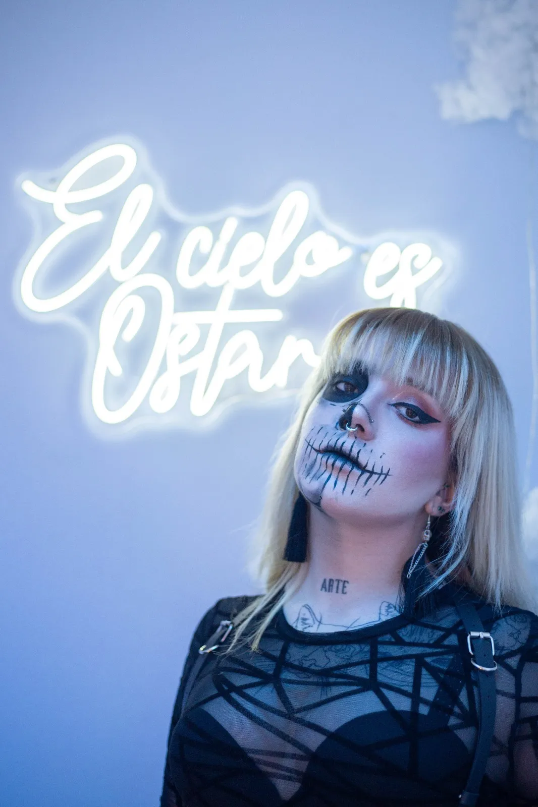 Mujer con maquillaje calaverico frente a pared con cartel "El cielo en Ostara"